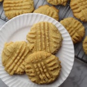 Three peanut butter cookies on a white plate with other cookies on a cooling rack in the background.