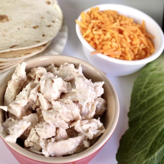 small bowl of chicken salad with cheddar cheese and tortillas in the background.