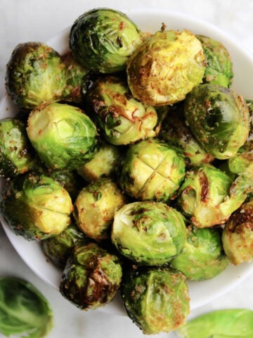 Brussels Sprouts in a white bowl. Skin is crispy with seasoning visible.