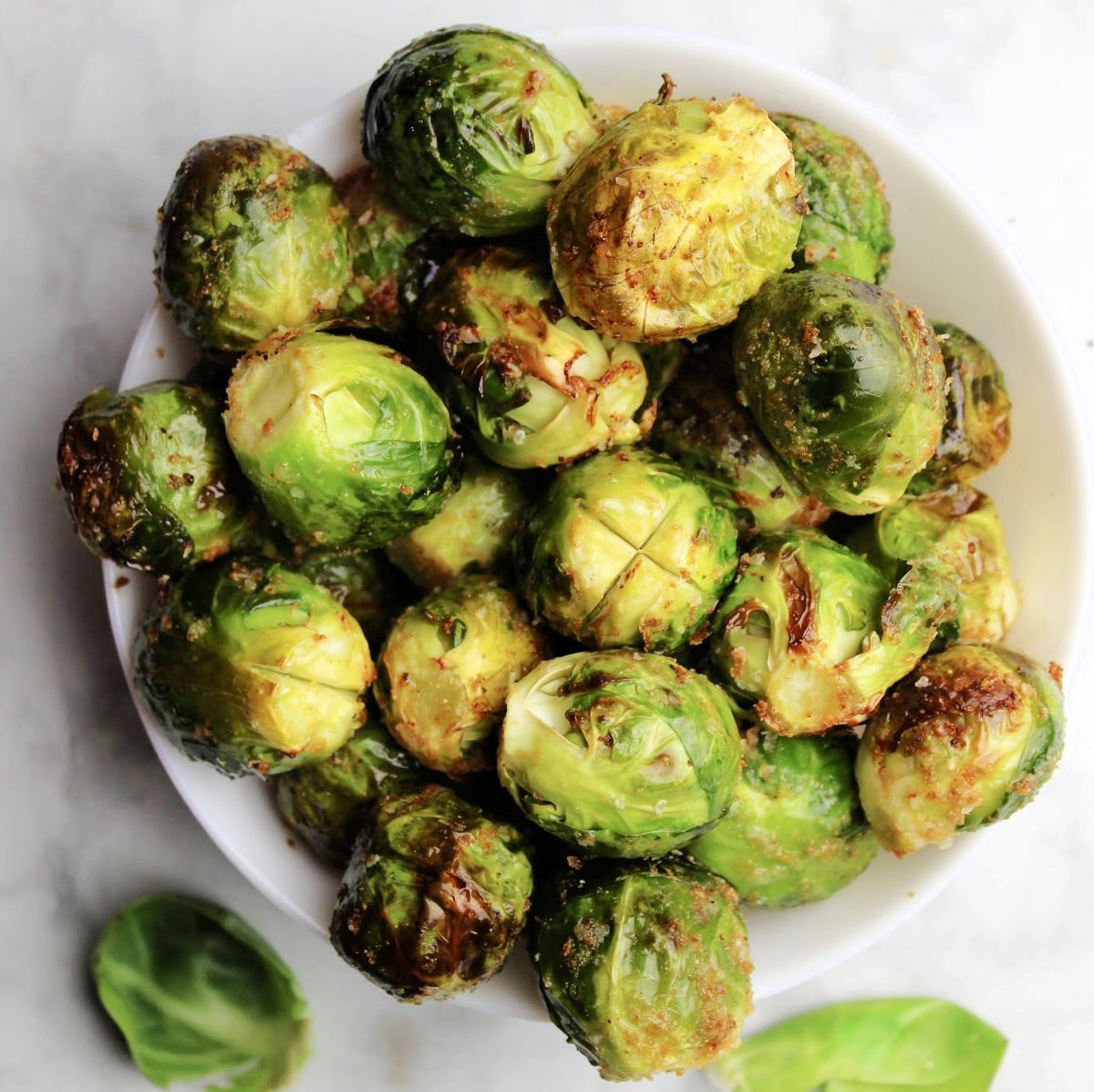 Brussels Sprouts in a white bowl. Skin is crispy with seasoning visible.