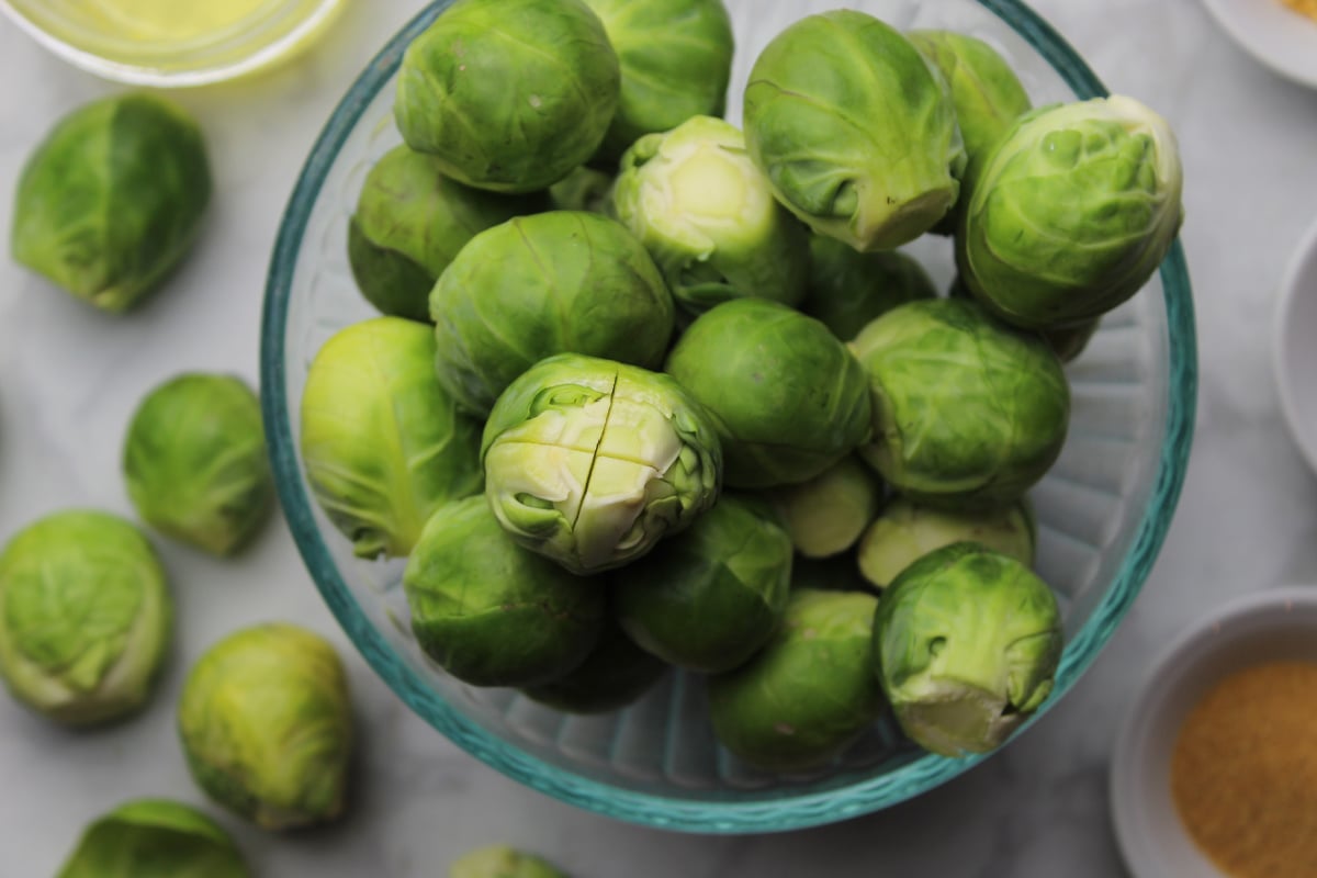 A bowl of Brussels sprouts with damaged outer leaves removed and an X cut into the stem.