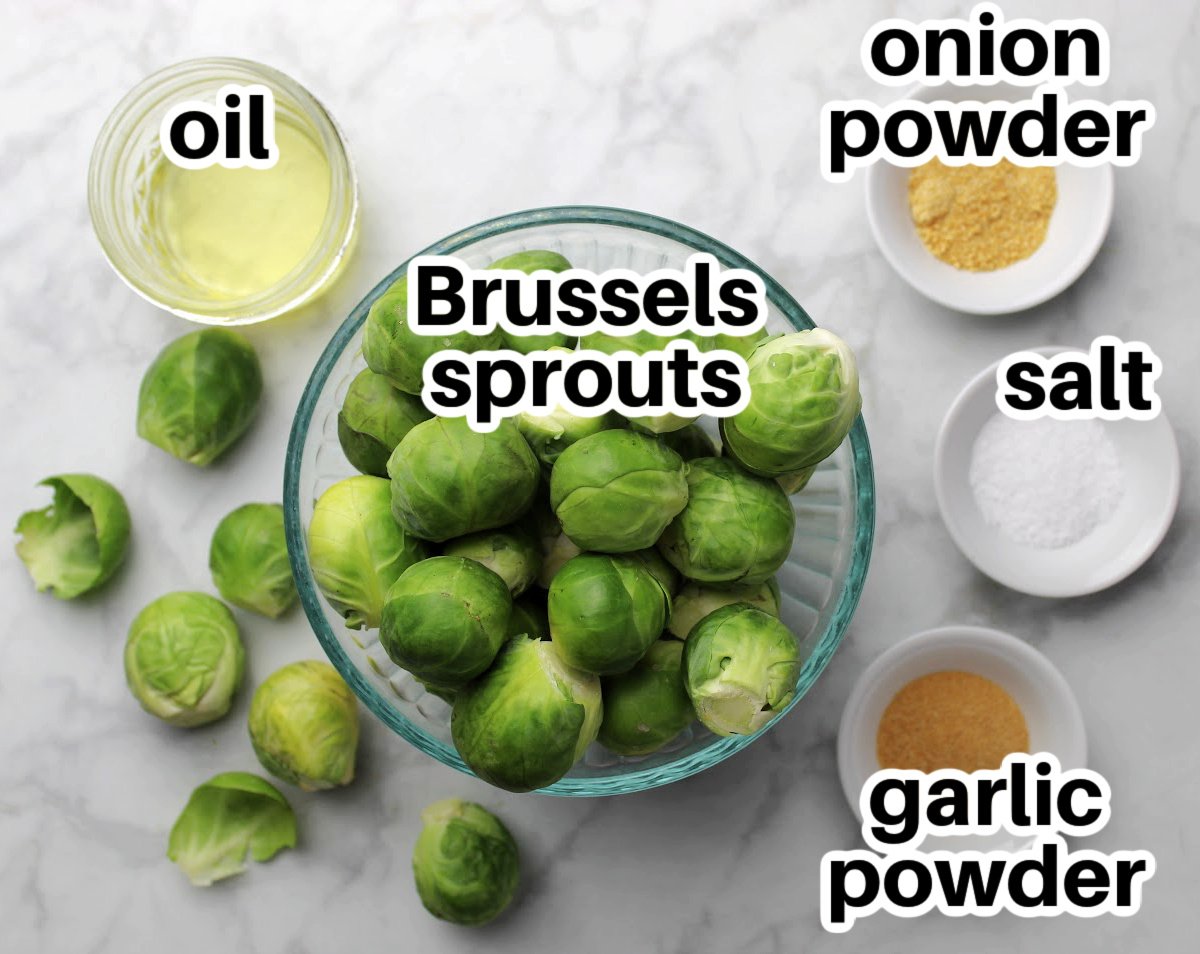 Brussels sprouts in a bowl, with small bowls containing onion powder, salt, garlic powder and oil.