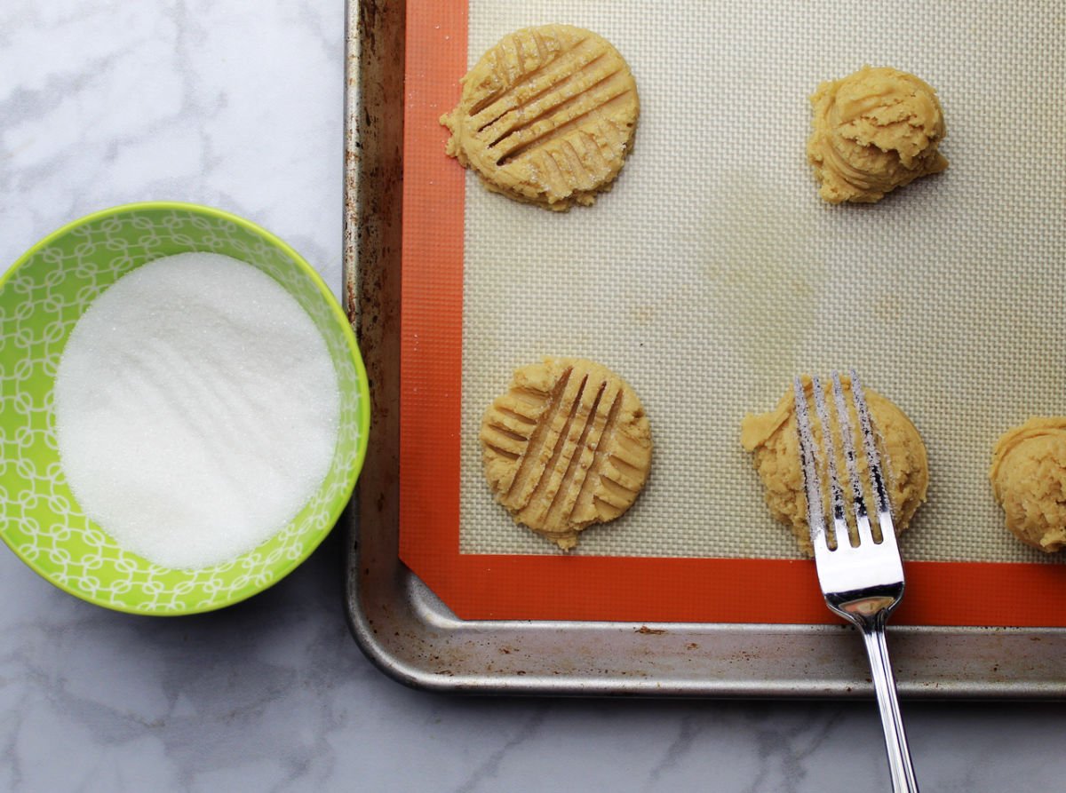 using a fork dipped in sugar to create traditional criss cross pattern on the peanut butter cookies