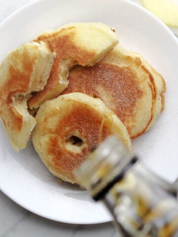 Apple ring pancakes with maple syrup being drizzled on them.