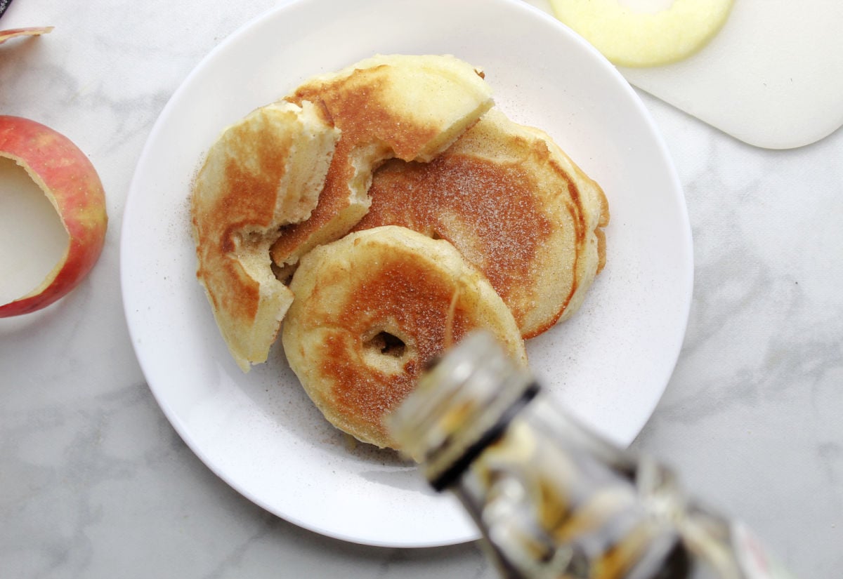 Apple ring pancakes with maple syrup being drizzled on them. 