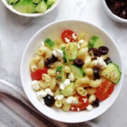 Greek pasta salad with lots of fresh toppings including cucumbers, tomatoes, olives, and feta cheese.