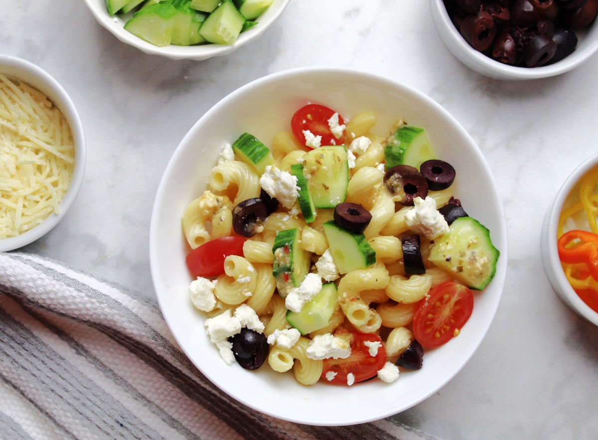 Greek pasta salad with lots of fresh toppings including cucumbers, tomatoes, olives, and feta cheese.