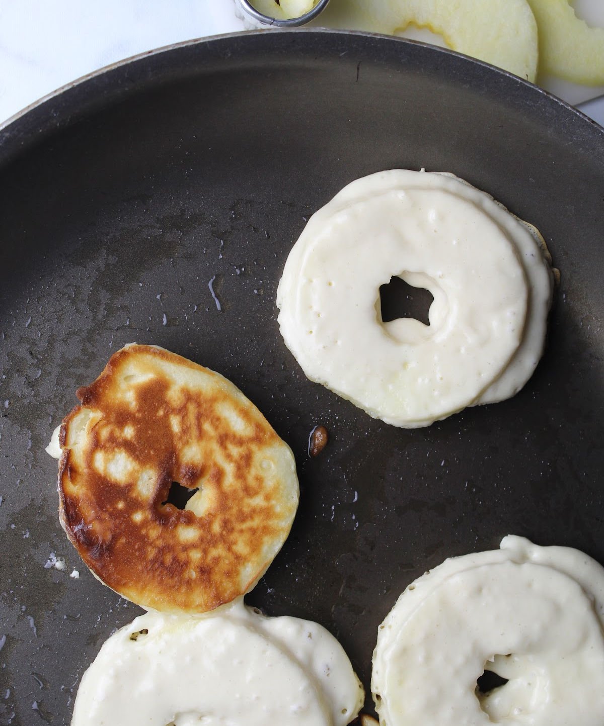 Apple pancake slices covered in pancake batter in a dark pan. 