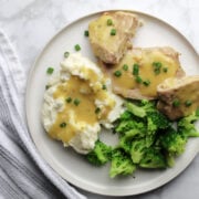 Ranch pork chop gravy on a plate with sides of gravy covered mashed potatoes and steamed broccoli