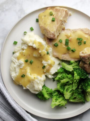 Ranch pork chop gravy on a plate with sides of gravy covered mashed potatoes and steamed broccoli