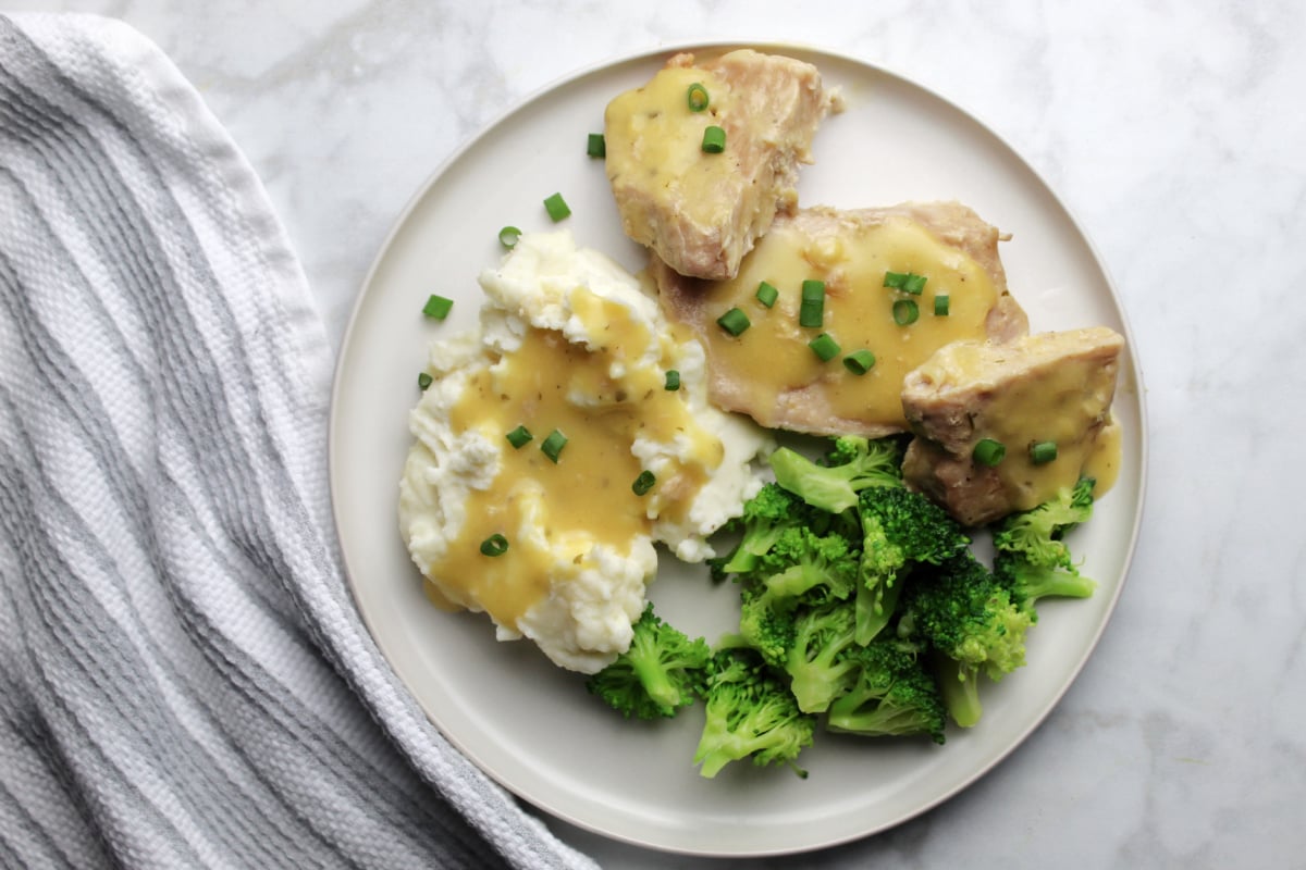 Ranch pork chop gravy on a plate with sides of gravy covered mashed potatoes and steamed broccoli