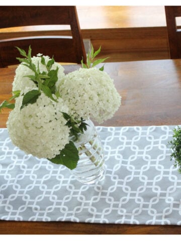A gray table runner with a vase of white flowers on it.