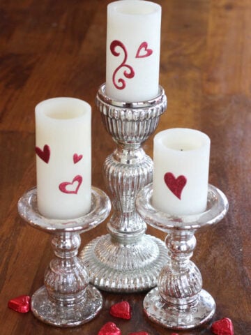 White candles with red heart stickers on them for Valentine's Day decor.
