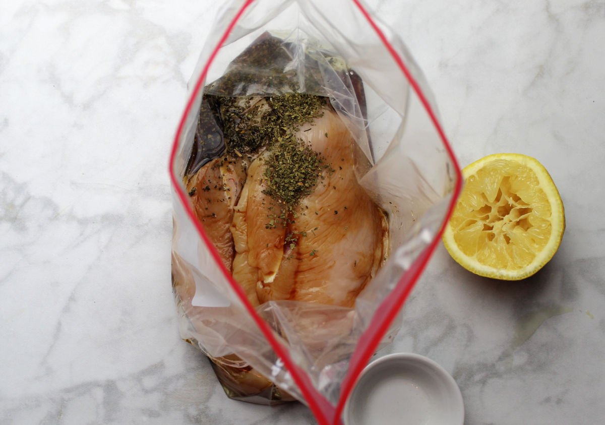 Chicken in a bag standing up so you can see into the bag.  Bag contains chicken, with lemon, soy, oil and oregano on top.