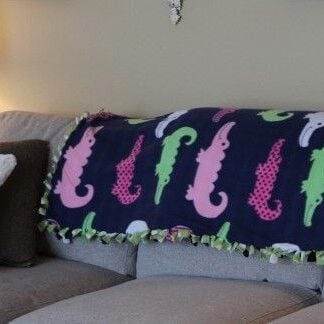 no sew fleece blanket that has a blue background and colored alligators draped on a neutral couch.
