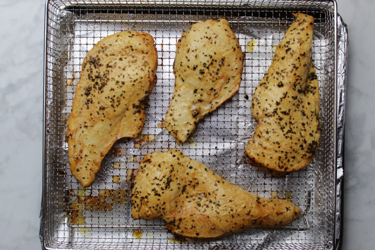An air fryer tray with four seasoned cooked chicken breasts.
