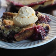 some blackberry dump cake topped with vanilla ice cream on a white plate.