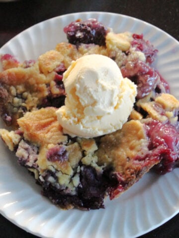A blackberry dump cake on a white plate with a scoop of ice cream.