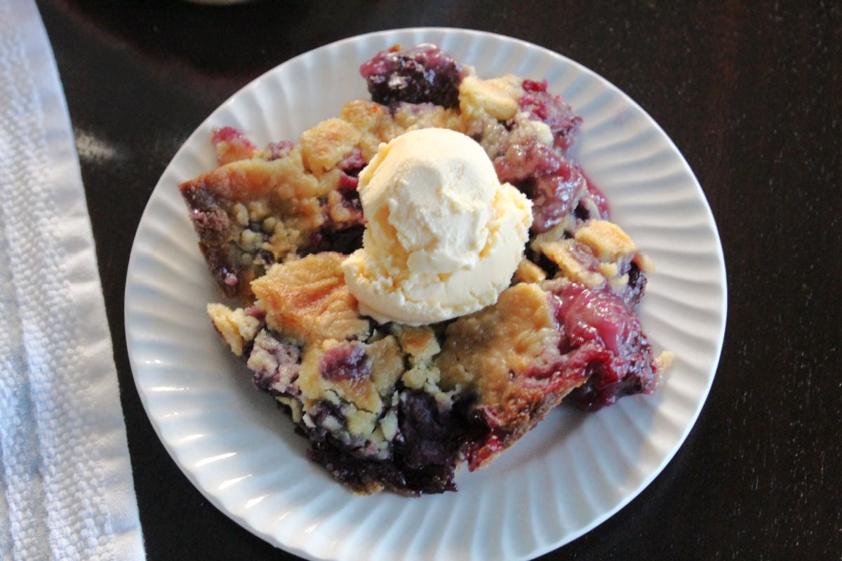 A blackberry dump cake on a white plate with a scoop of ice cream.