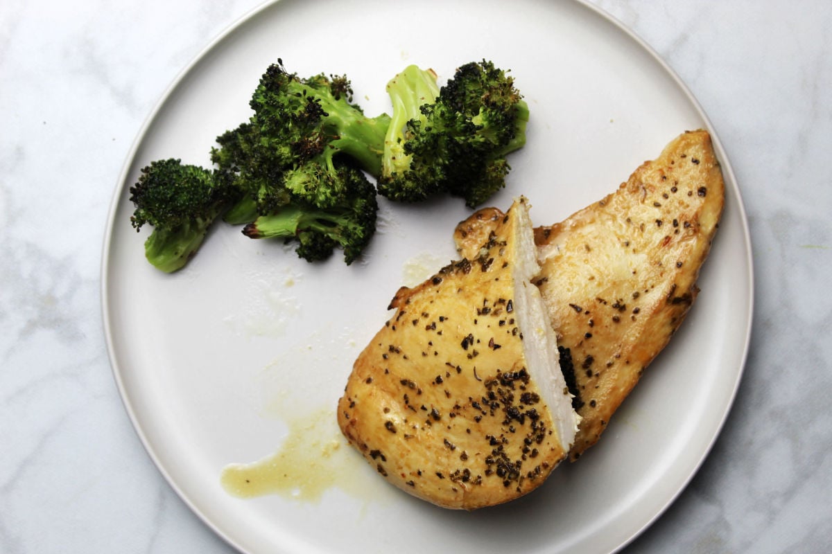 A juicy seasoned chicken breast on a plate with roasted broccoli as a side. 