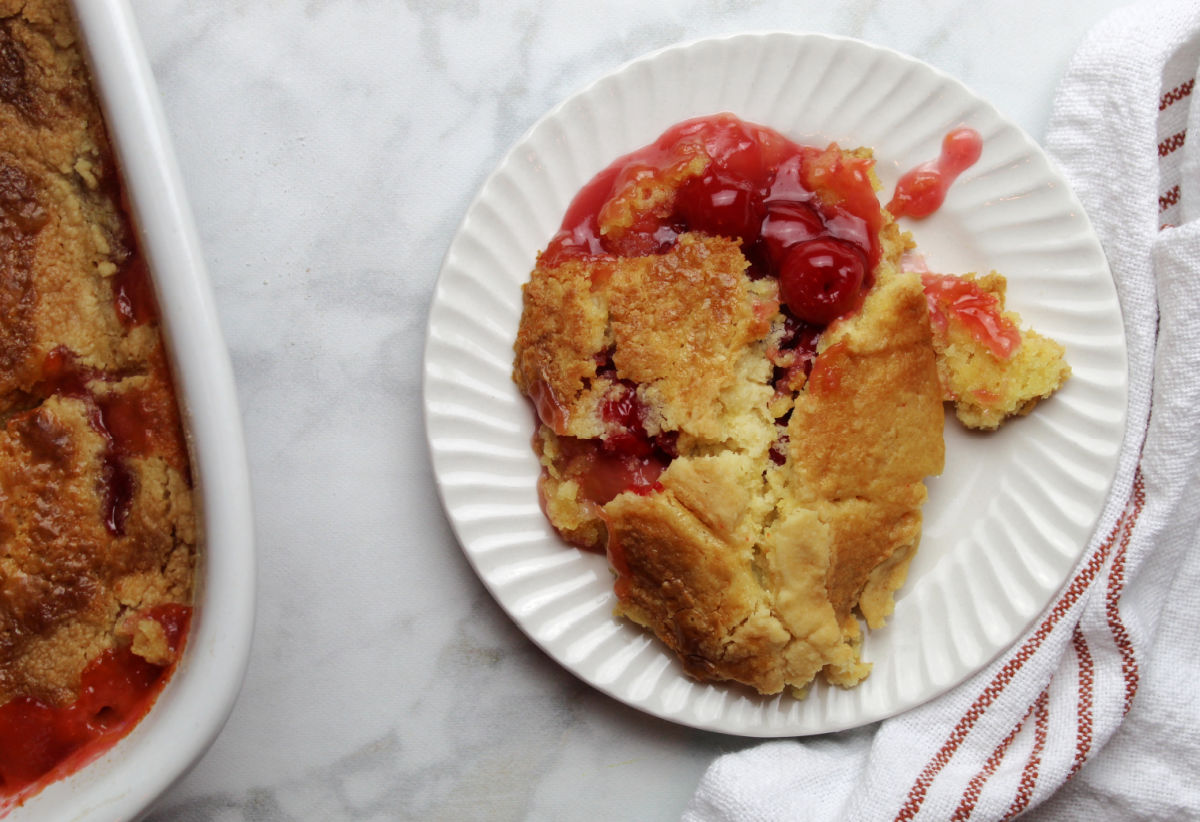 A piece of cherry pineapple dump cake. It looks like a cobbler with a delicious topping with pie cherries peeking through the topping.