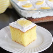 lemon poke cake with white whipped topping garnished with a ¼ slice of lemon.