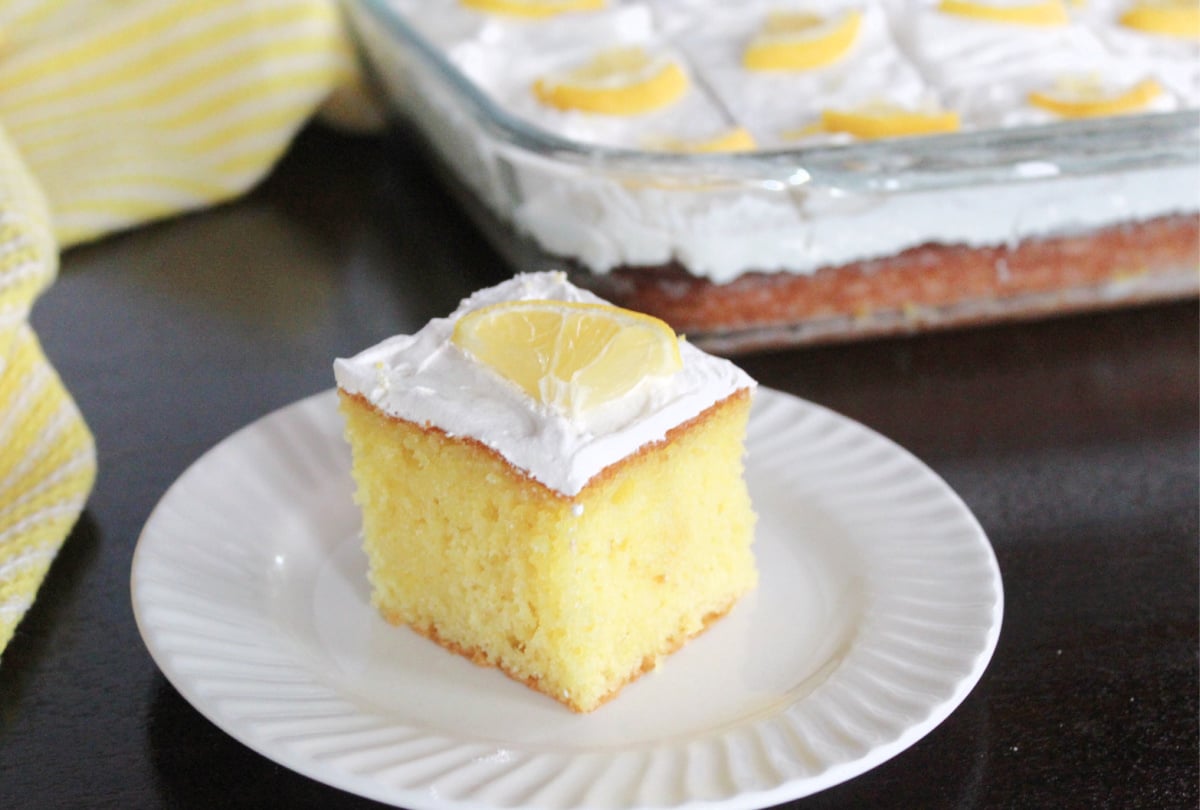 yellow lemon cake square with white whipped topping garnished with a ¼ slice of lemon.