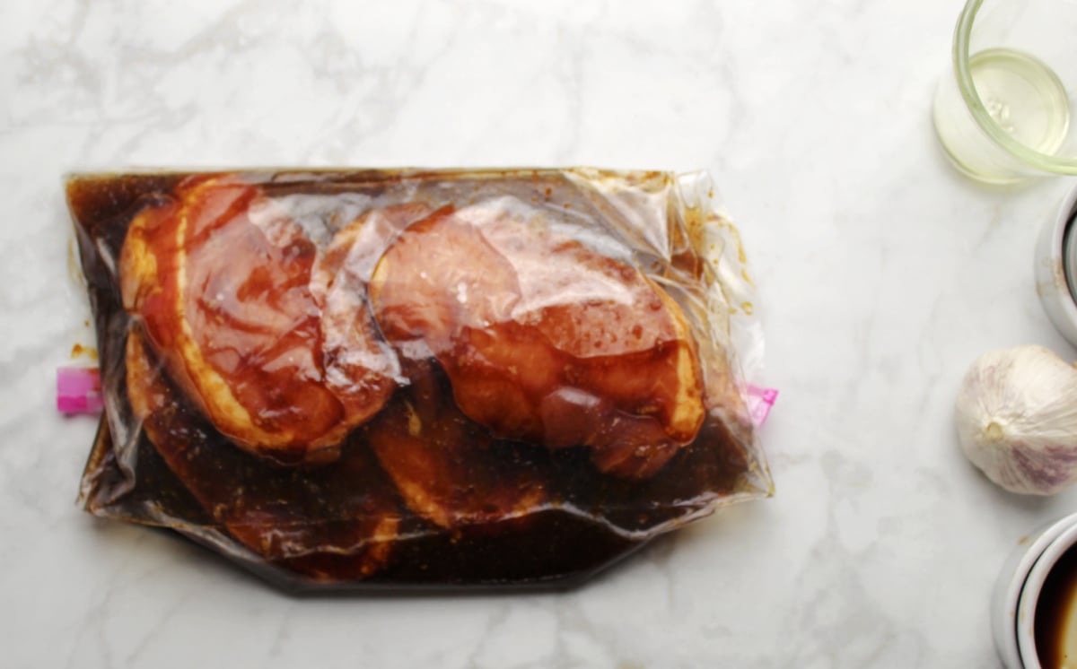 Pork chops marinading in a dark liquid in a zip bag.