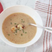 Cauliflower soup with roasted cauliflower as garnish served in a white bowl.