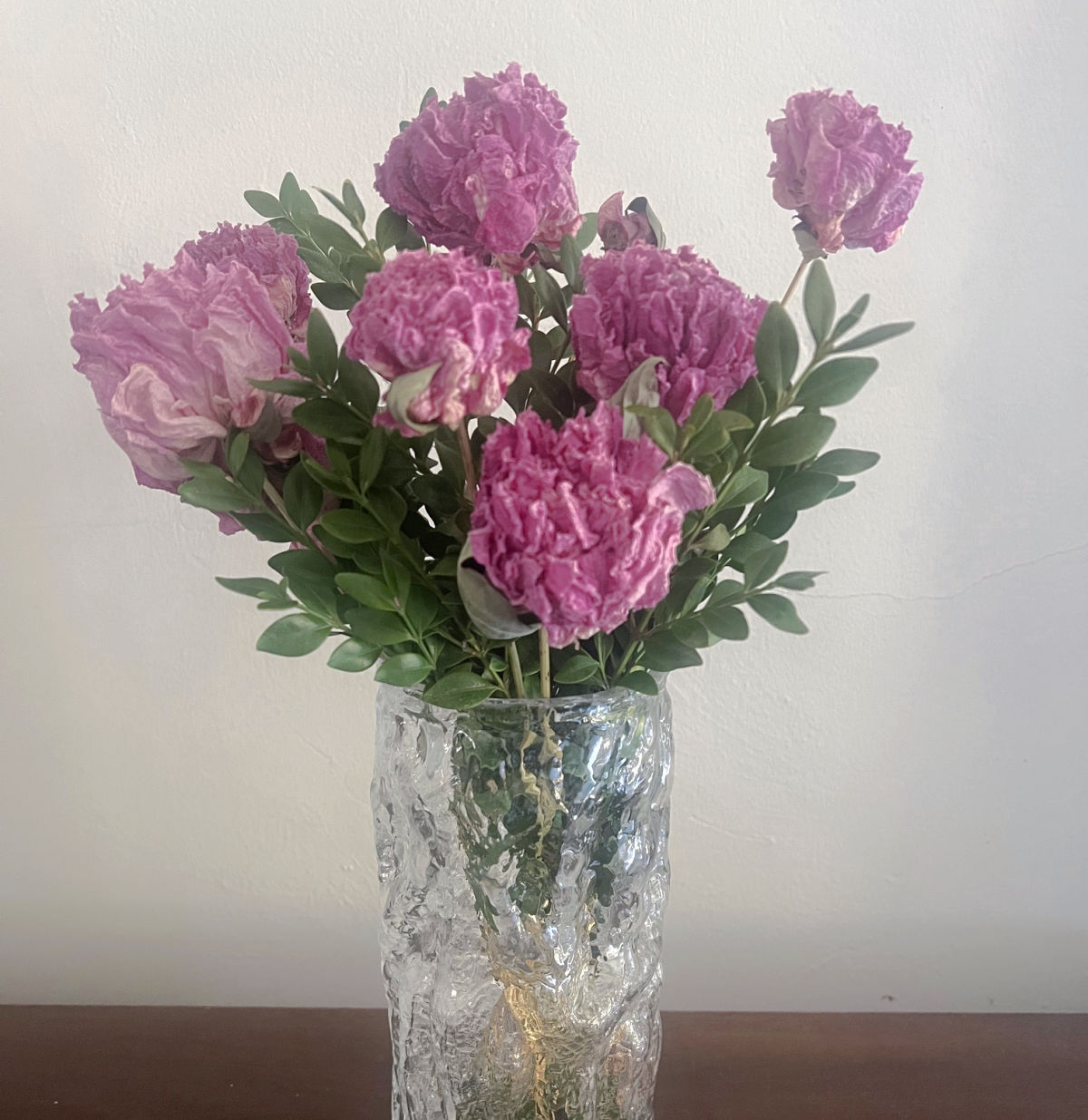 some beautifully dried pink peonies with some fresh green boxwood clippings in a clear vase.