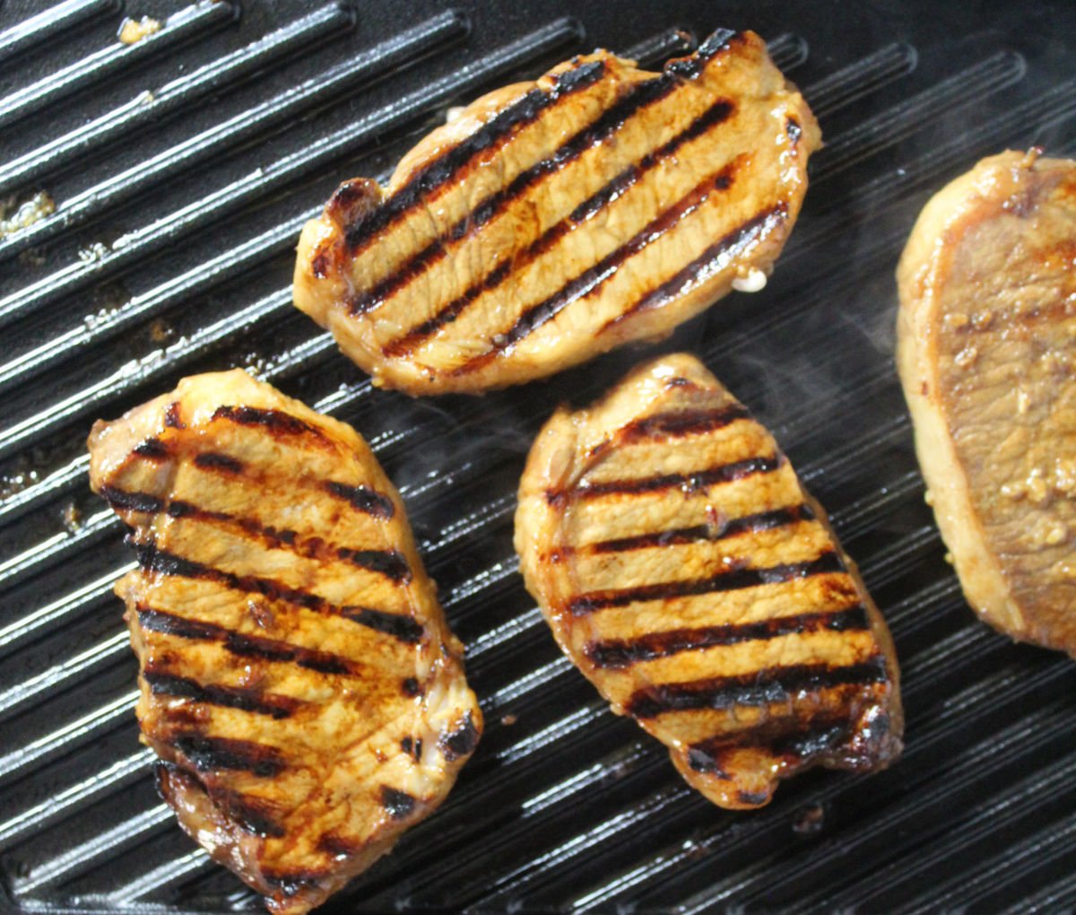 Pork chops being grilled.  Grill marks are seen on three pork chops.