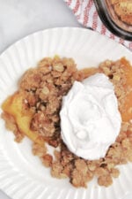 peach crisp on a white plate with whipped topping.