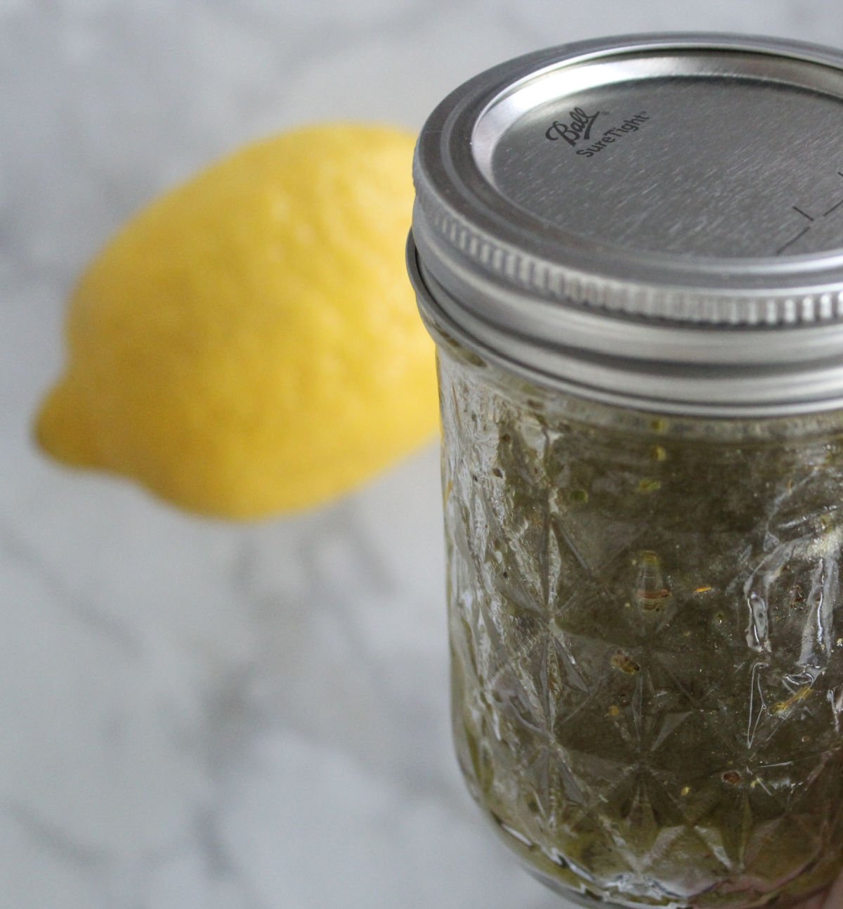 A mason jar containing three ingredient Greek salad dressing. Lemon in the background.