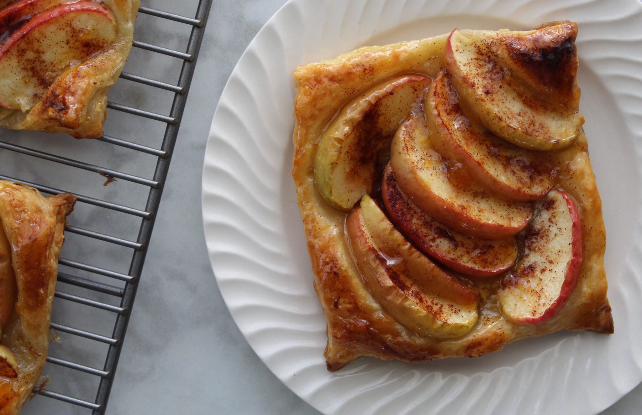 Puff pastry apple tart on a white plate.  Other apple tarts can be seen cooling to the side.