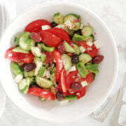 Greek salad in a white bowl. Fresh and appetizing ingredients include cucumbers, tomatoes, green peppers, olives and red onions