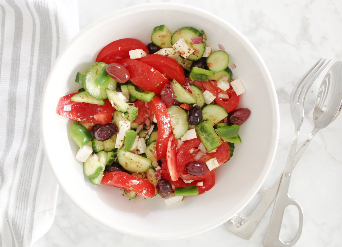 Greek salad in a white bowl. Fresh and appetizing ingredients include cucumbers, tomatoes, green peppers, olives and red onions