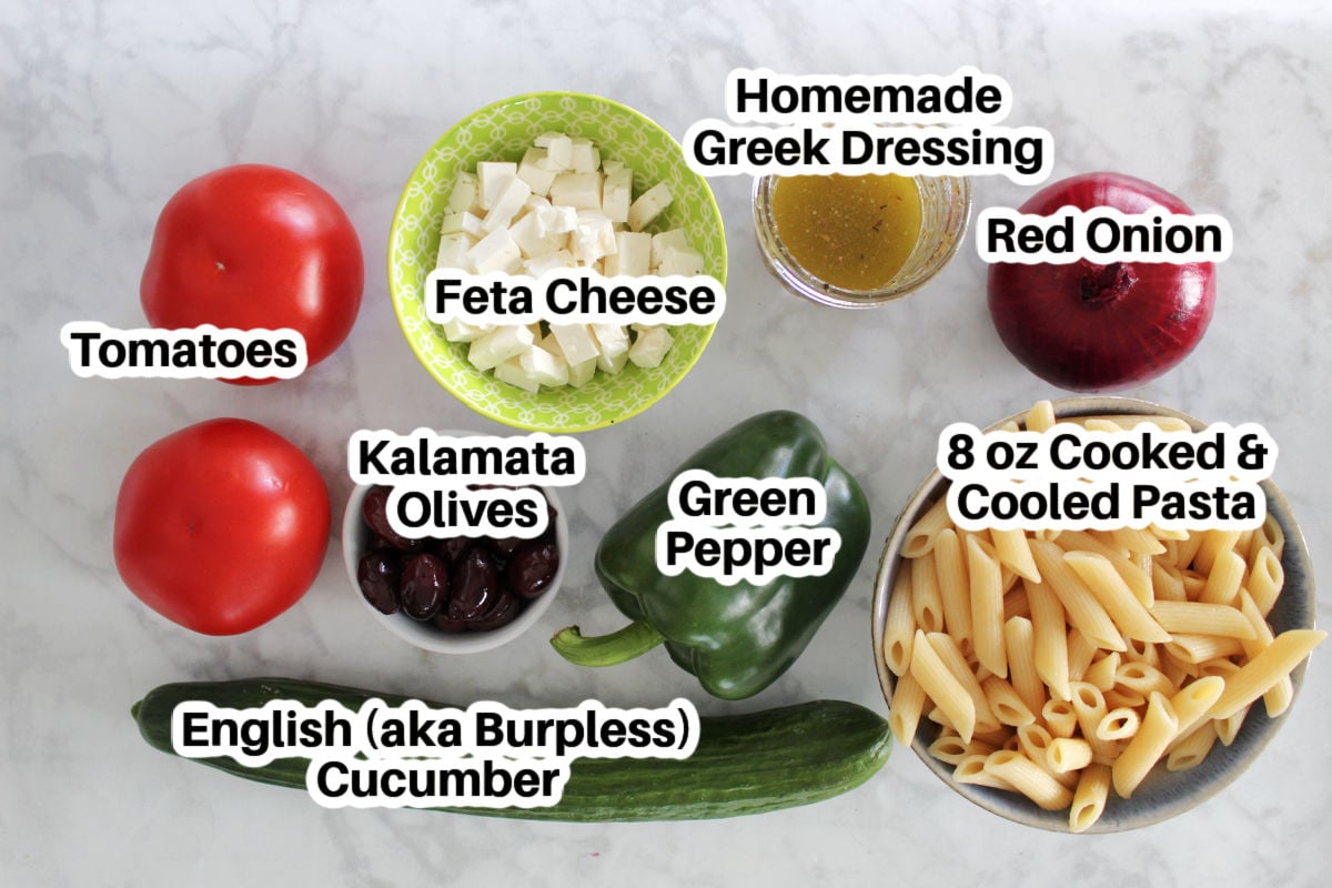 Ingredients for Greek Pasta Salad which includes tomatoes, feta cheese, kalamata olives, green peppers, English cucumber, red onion, cooked and cooked pasts andmy homemade 3 ingredient greek pasta.