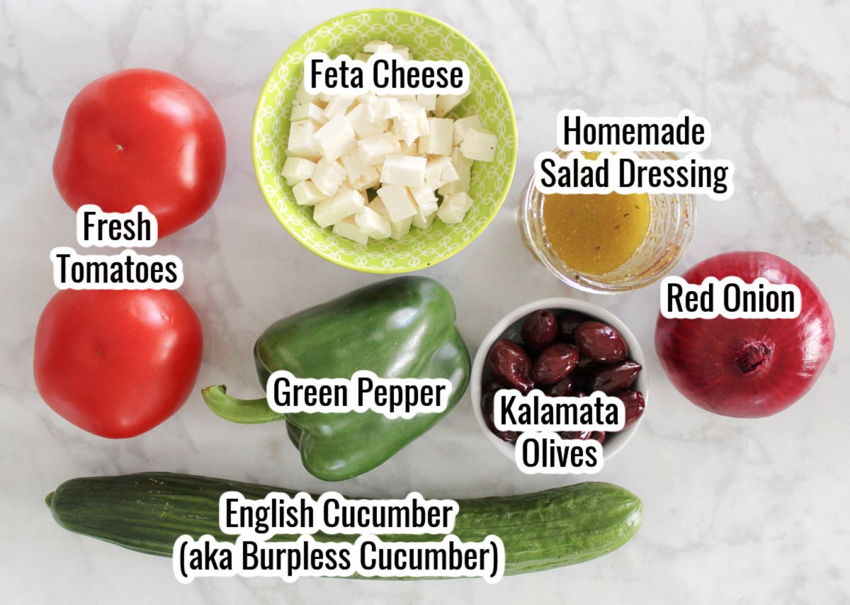 Greek Salad ingredients including cubed feta cheese, tomatoes, green pepper, English cucumber, red onion, Kalamata Olives, homemade salad dressing