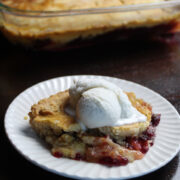 delicious portion of apple cranberry dump cake with a scoop of vanilla on top. On a white plate sitting on a dark wooden table.