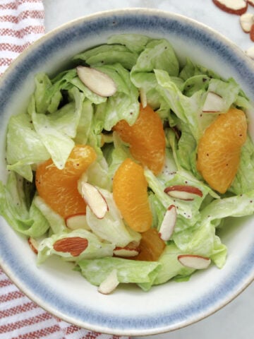 Mandarin orange salad in a bowl. Salad contains lettuce, mandarin oranges, poppyseed dressing and juicy slices of mandarin oranges.