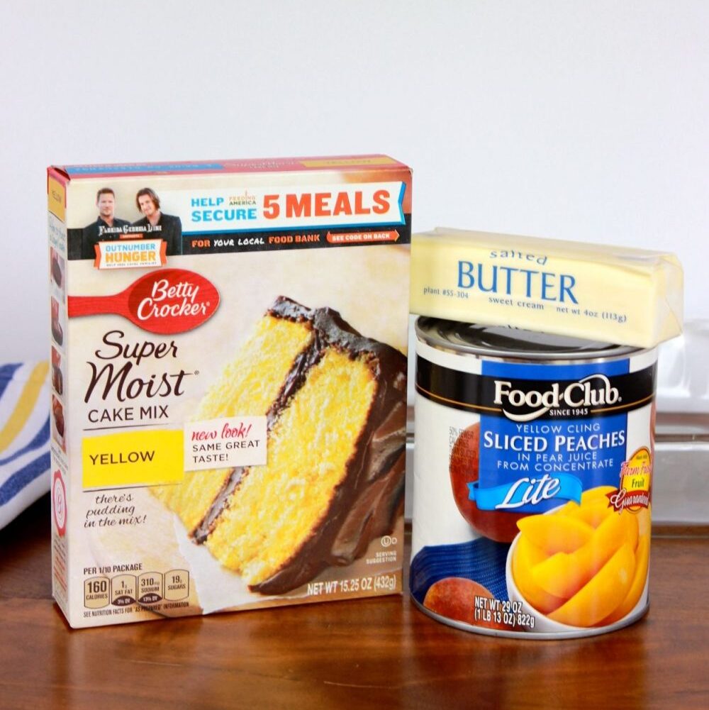 three ingredient peach cobbler ingredients that include a yellow cake mix, a large can of sliced pumpkins and a stick of butter.