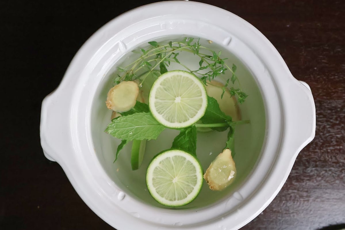 simmer pot containing lime slices, fresh mint leaves, fresh thyme springs and sliced fresh ginger.