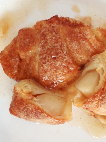 two apple dumplings on a plate with one cut open so you can see the apples in the baked crescent roll.