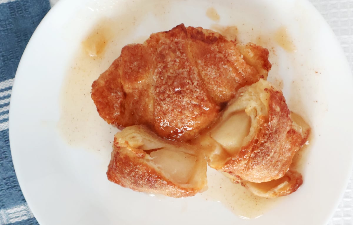 two apple dumplings on a plate with one cut open so you can see the apples in the baked crescent roll.