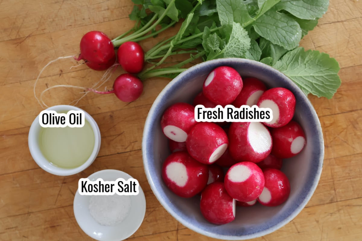 a bowl of cleaned radishes, some radishes with their leaves on them in the upper part of the picture, a small white contianer of olive oil and another small container with kosher salt. 