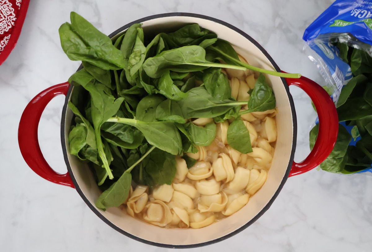 tortellini and fresh spinach added to simmering broth.