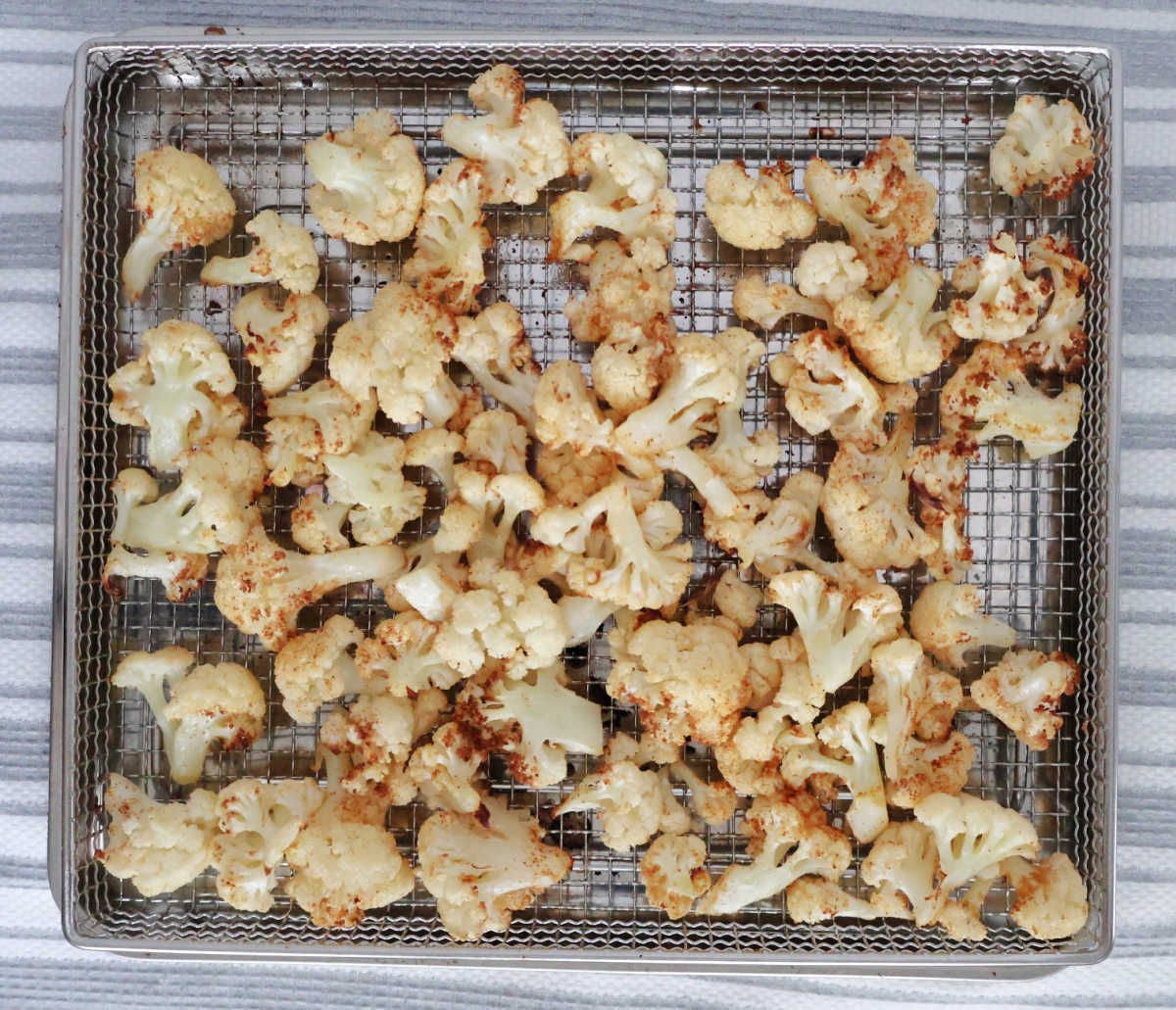 Air fryer tray with roasted and seasoned cauliflower florets.