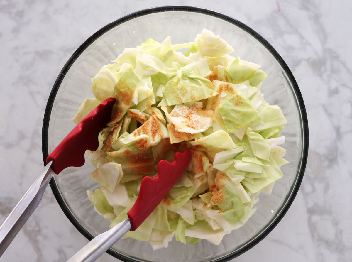 using tongs to toss seasonings, oil and vinegar with chopped  cabbage.