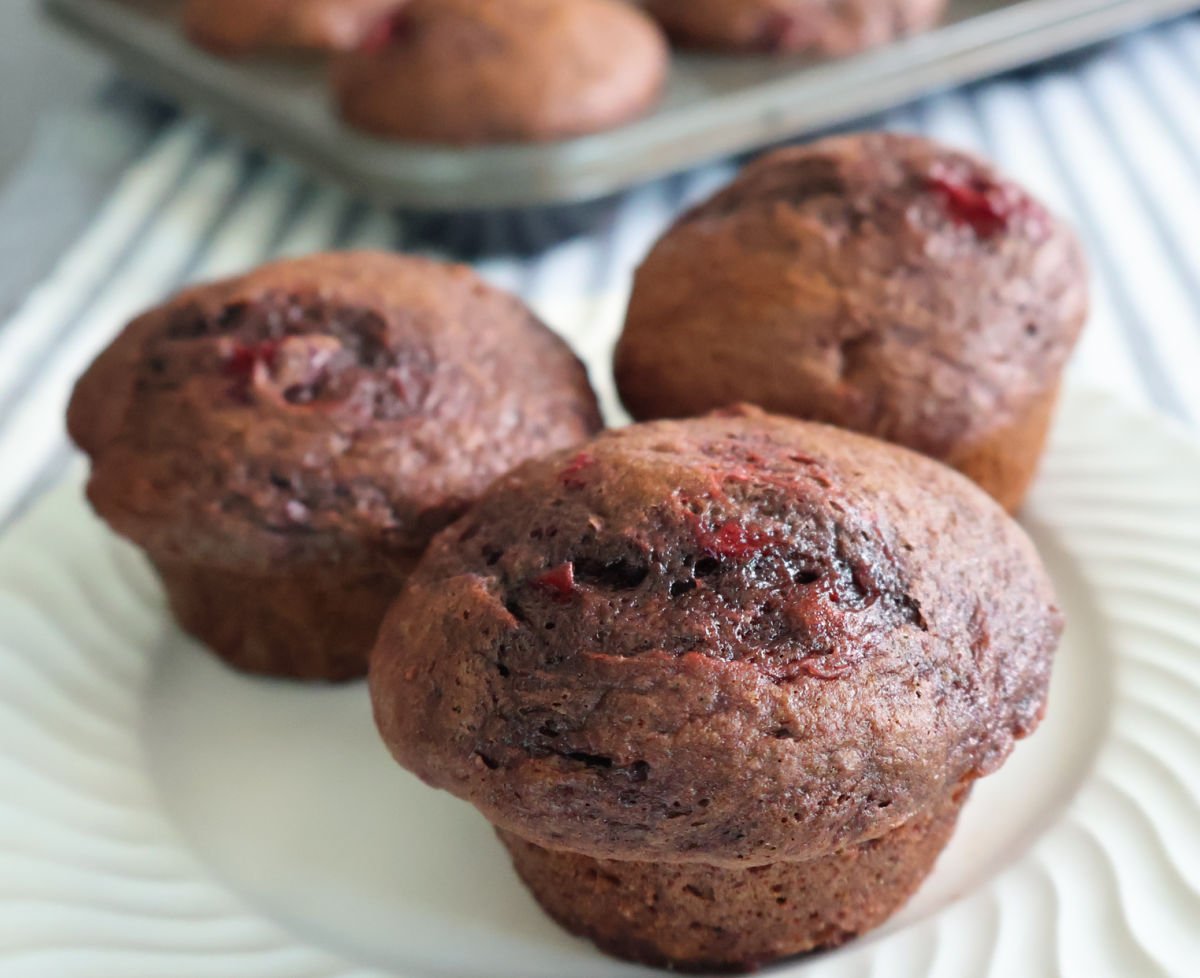three chocolate cherry muffins on a white plate.