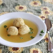 Three matzo balls in broth in a wide rimmed white soup bowl.